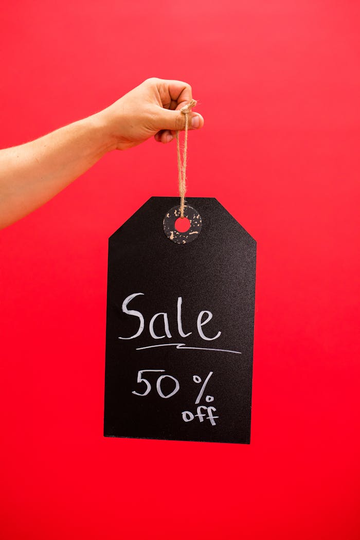Hand holding a black sale tag with 50% off on a red background.