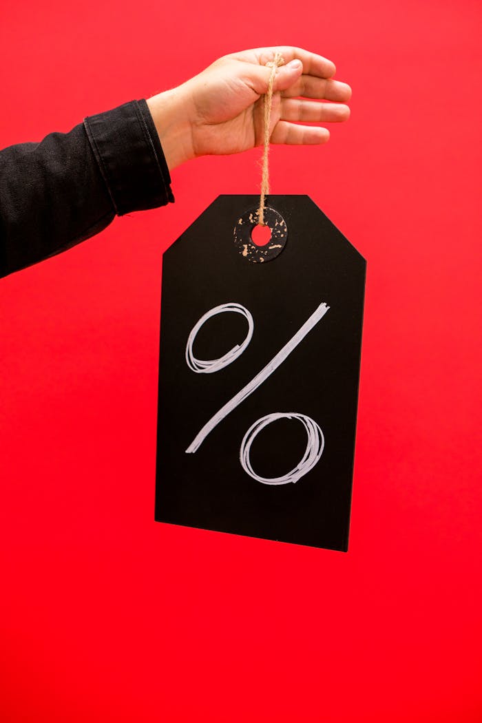 Stylish hand holding a sale tag with a percentage sign on a vibrant red backdrop.
