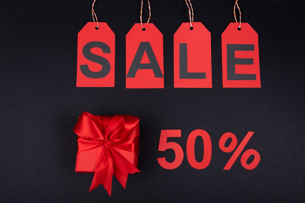 Red gift box next to sale tags and 50% sign on black background, ideal for promotions.